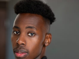 A headshot of a young black man wearing a black turtleneck.