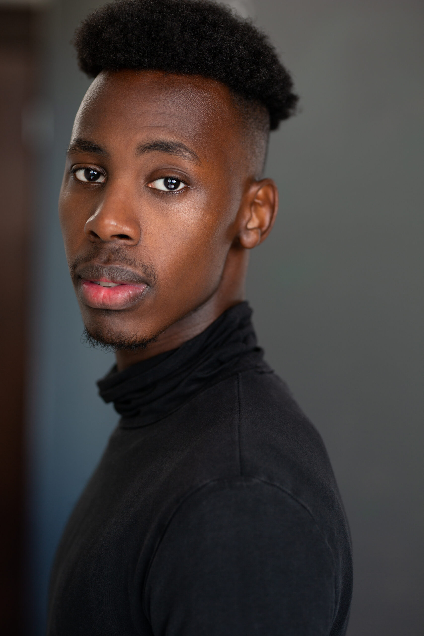 A headshot of a young black man wearing a black turtleneck.