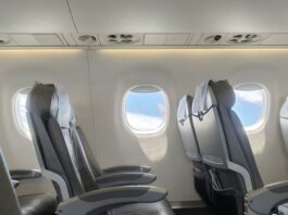 Empty airplane cabin. You can see two rows of two seats and the clear skies out of the windows.