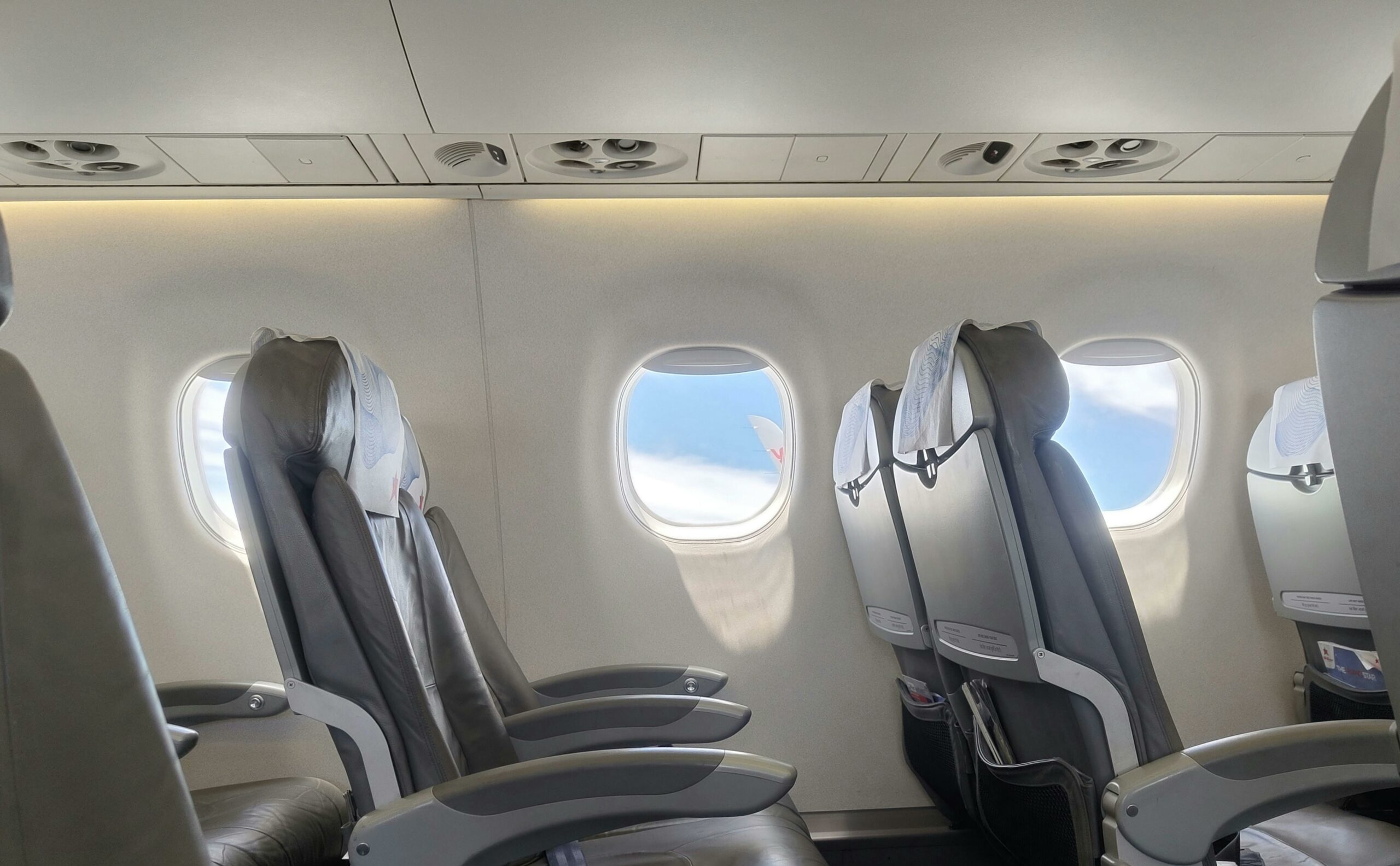 Empty airplane cabin. You can see two rows of two seats and the clear skies out of the windows.