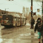 Peakie helps you navigate the aftermath of the atmospheric river 99 B-Line bus crossing an intersection on a rainy day. There are pedestrians wearing masks who are crossing as well.