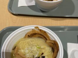 A bowl of noodles topped with charred meat, beansprouts, bamboo shoots, and chopped mushrooms.