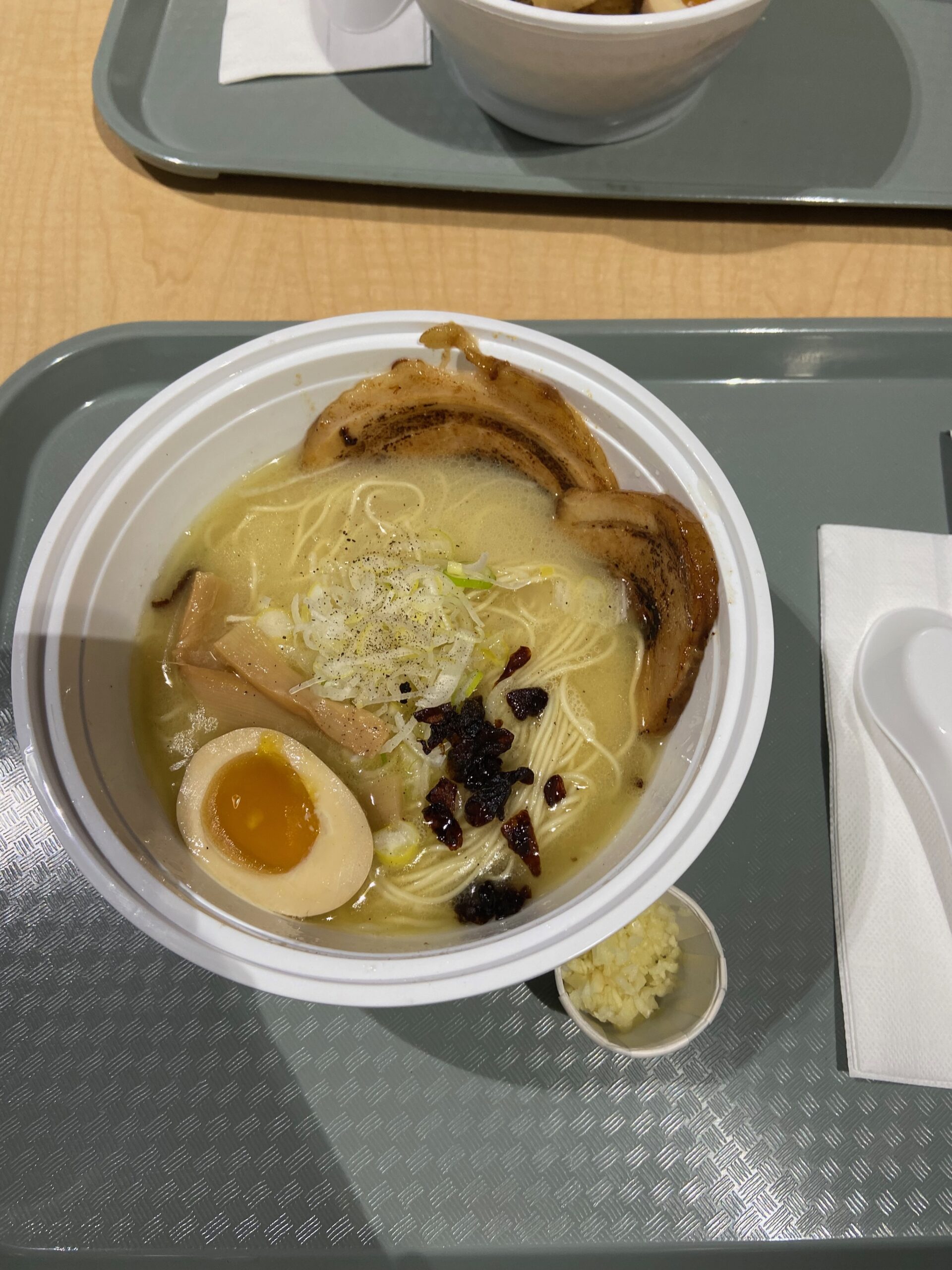 A bowl of noodles topped with charred meat, beansprouts, bamboo shoots, and chopped mushrooms.