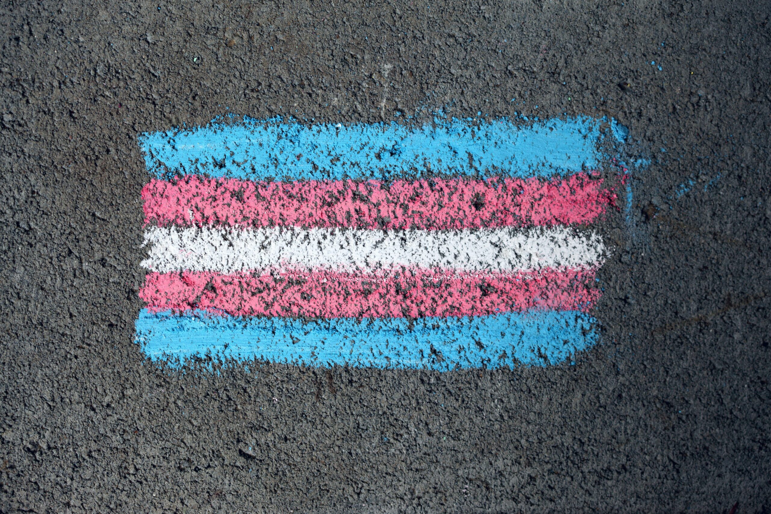 Chalk lines of blue, pink, white, pink again, and blue again drawn on concrete depicting a trans flag.