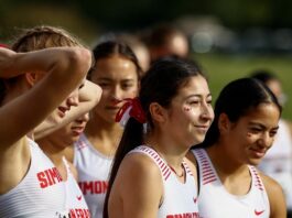 A group of girls wearing white uniforms with red lettering. The words “Simon Fraser” sit at the top of their shirts.