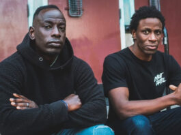 A close-up of two black men wearing black and sitting on the steps of a school.