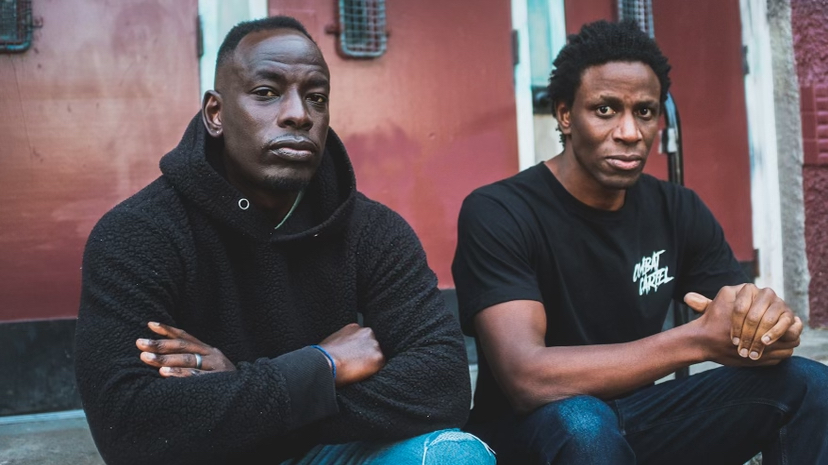 A close-up of two black men wearing black and sitting on the steps of a school.