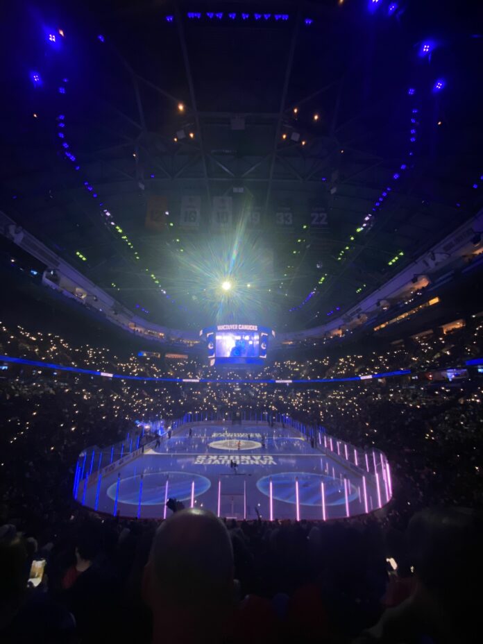 The inside of a hockey rink lit up in blue and purple as well as individual phone lights.
