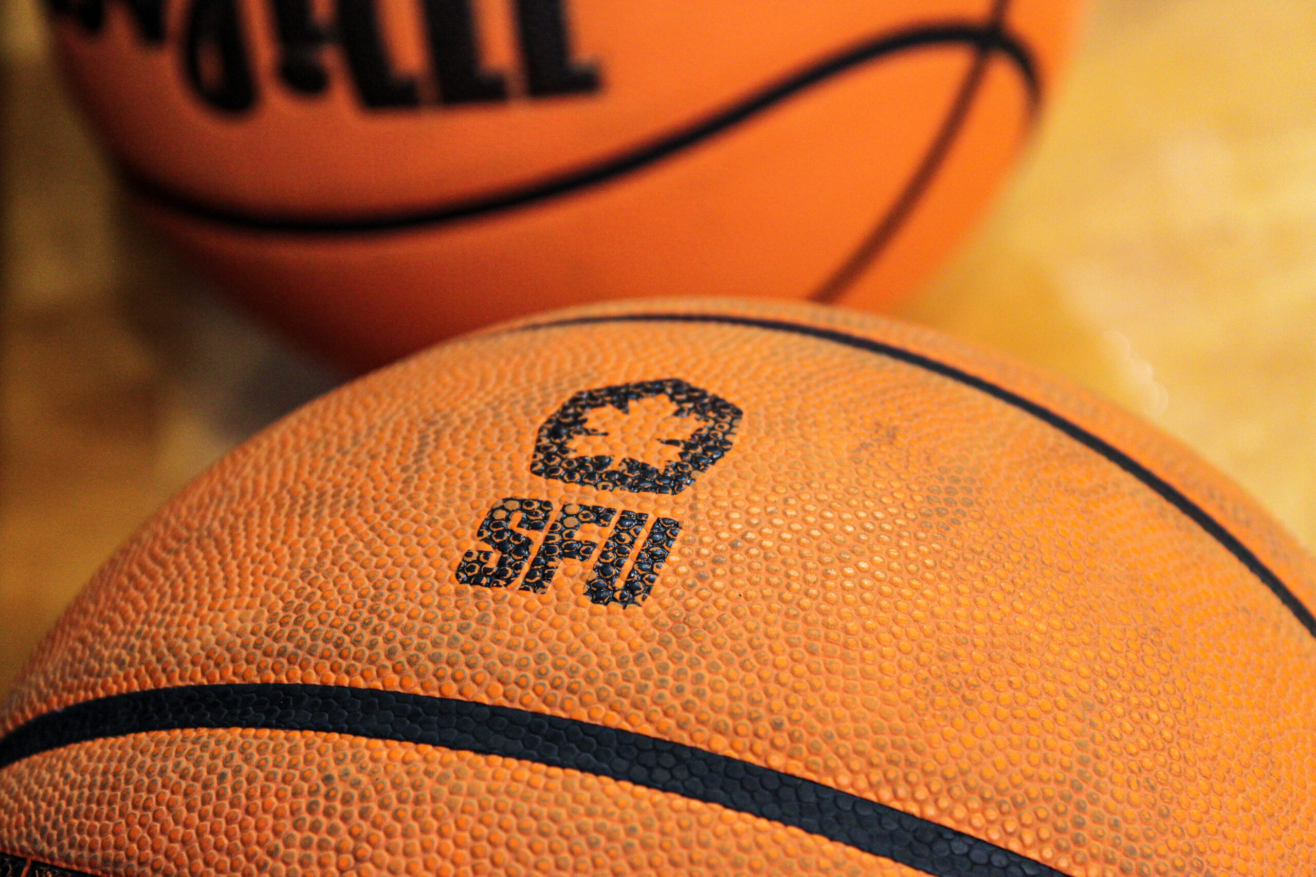 A close-up of an orange basketball with the ‘SFU Red Leafs’ logo at the focal point, stamped in black.