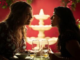 Two women face each other from separate ends of a restaurant table. In the background, a white water fountain can be seen.