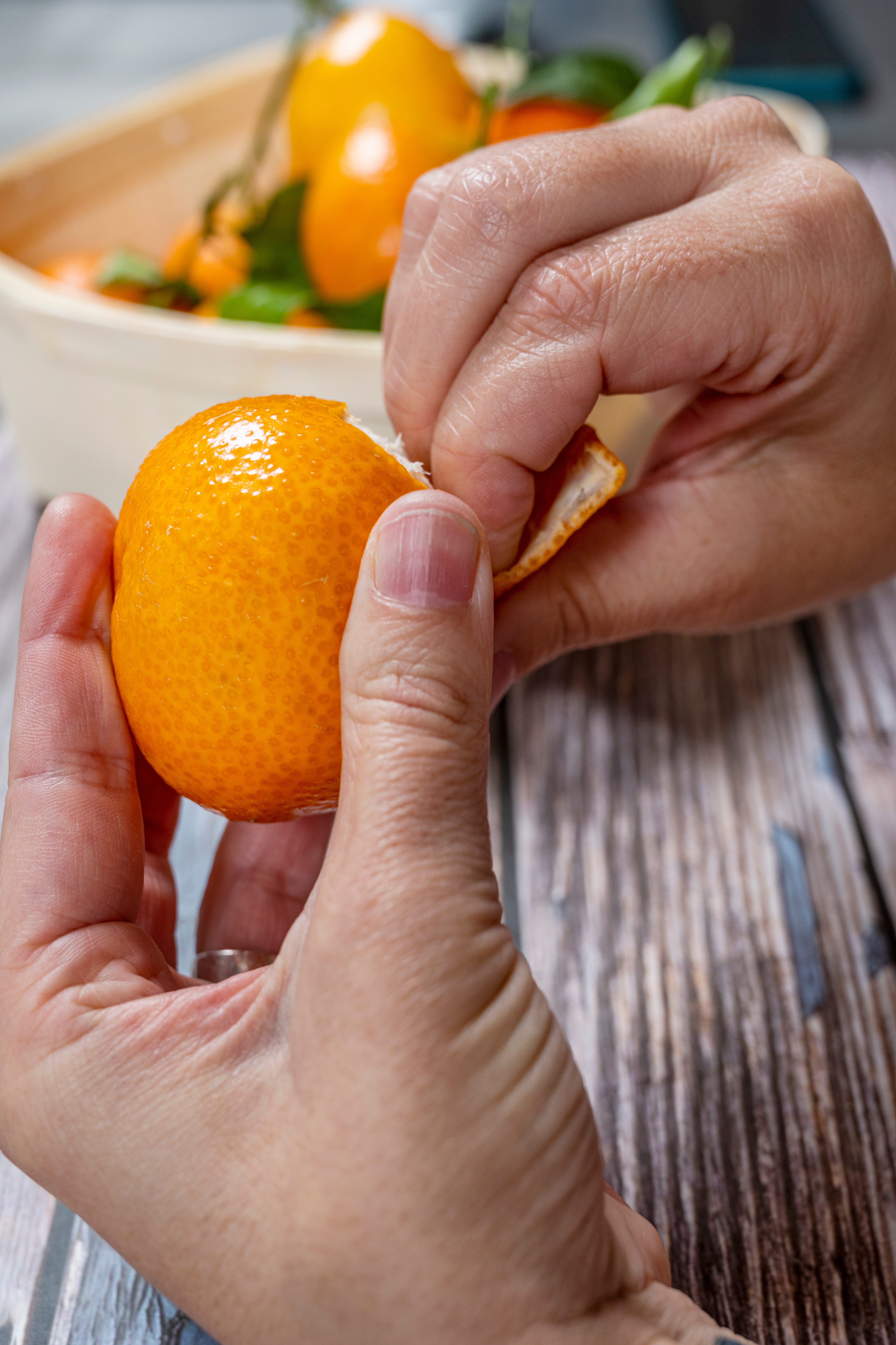 a pair of hands struggle to peel a mini orange