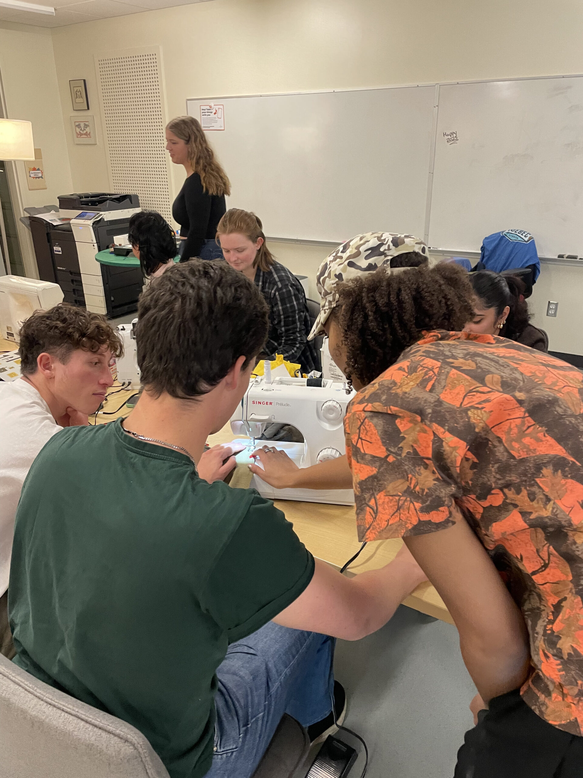This is a photo of seven students gathered around a table and sewing machine at the workshop.