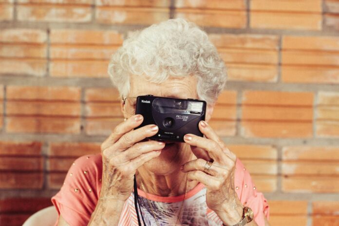 An old woman holds up a camera as she photographs herself in the mirror