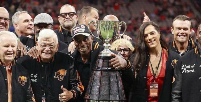 A group of people posing for a photo with the Grey Cup, including a woman with brown hair directly to the trophy’s right.