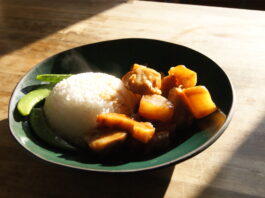 A black plate with a steaming scoop of rice, green beans, and brown chunks of vegetables.