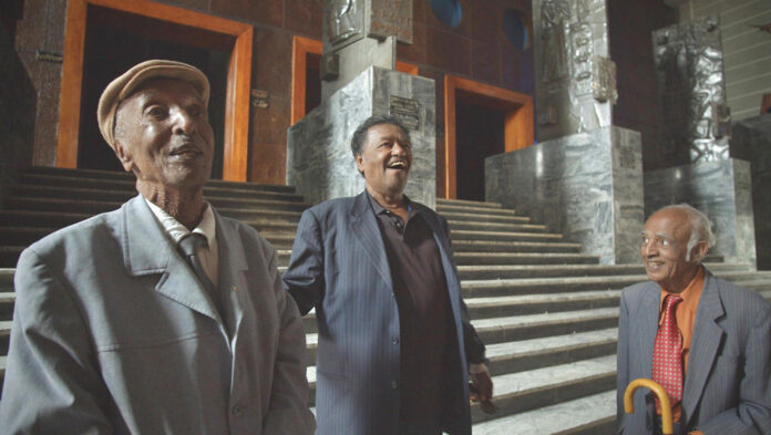 Three older men laugh while staring out at something past the camera lens.