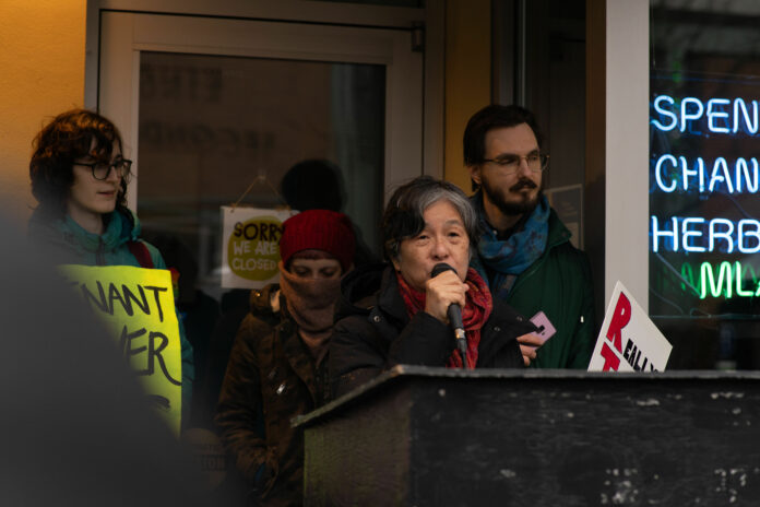 feature_VTU_-13 This is a photo of Abby Leung speaking into a mic, where members of the VTU stand behind her in support.