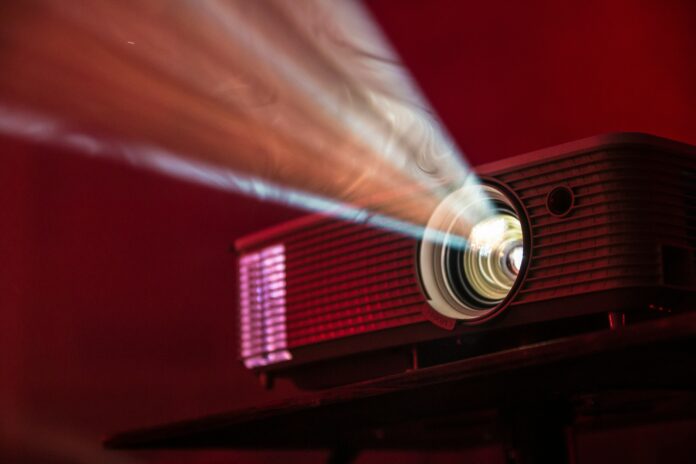 ntkntg-projector-alex-litvin-unsplash A film projector shines a light through a dark space.