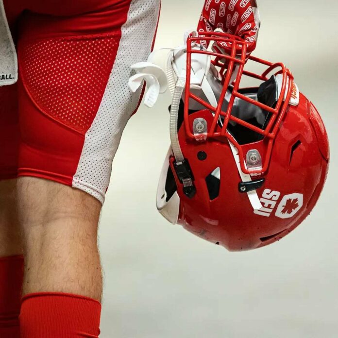 This is a photo of an SFU football player holding his helmet to the side of his body, with the photo facing from the back.