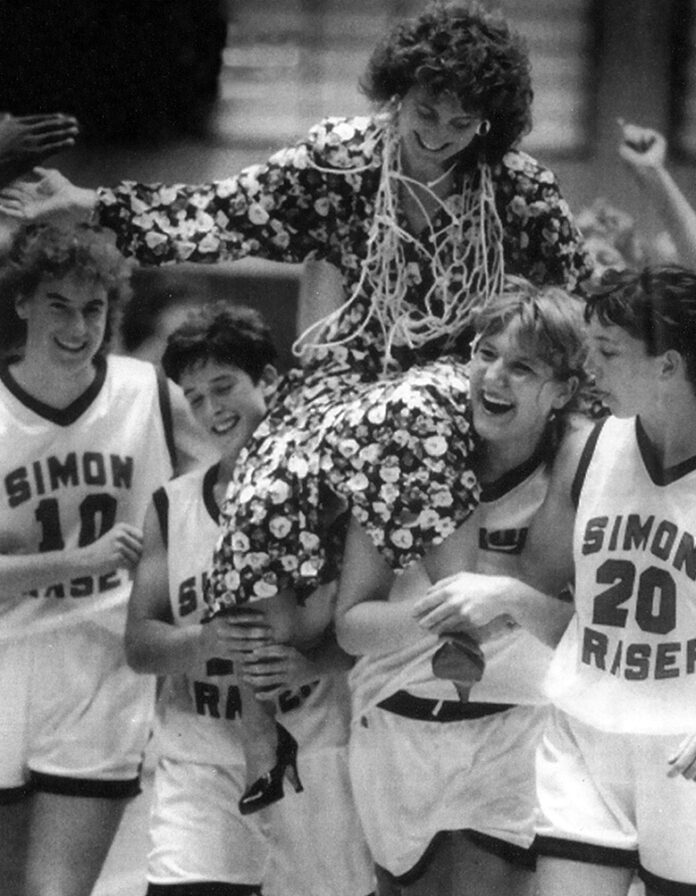 A woman is carried by a bunch of women basketball players in SFU uniforms. Draped over her is the netting from a basketball hoop.