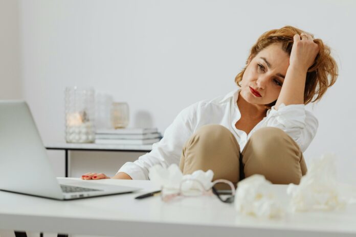 Woman sitting in front of her laptop looking upset. She’s surrounded by used tissues.