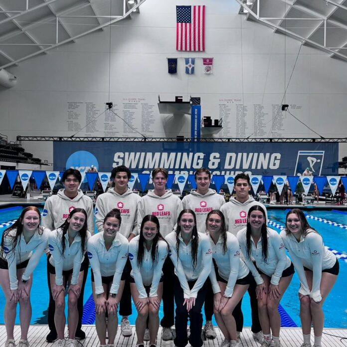 The SFU swim team stands in front of an indoor pool. On the back wall are the words “swimming and diving.”