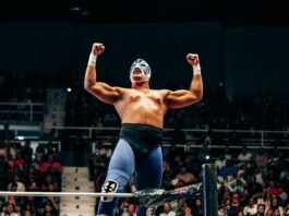 Masked wrestler throwing his arms up triumphantly in the ring.