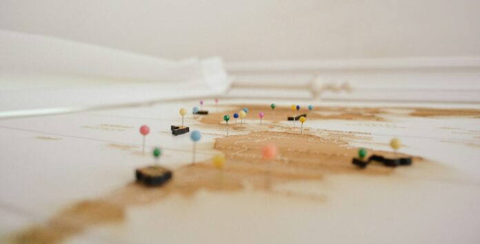 delfi-de-la-rua-map-unsplash A side view of a map with multiple different coloured thumbtacks pushed in.
