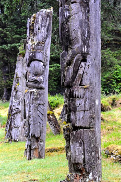 This is a photo of three Haida Gwaii totem poles with greenery in the background.