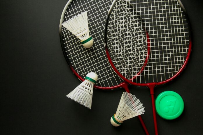 Two badminton racquets laying against a black background. Three birdies are sprawled around them.