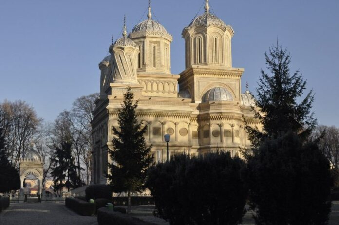 this is an aerial-view photo of the Curtea de Argeş cathedral in Romania. The castle is square shaped and has five spired towers.