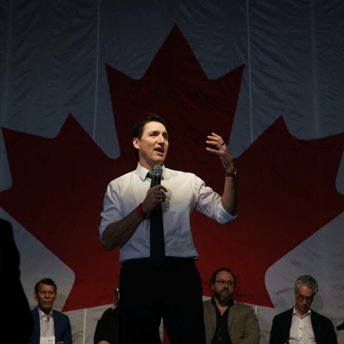 This is a photo of former prime minister Justin Trudeau standing before a Canadian flag.