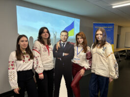 This is a photo of four Ukrainian students standing around a cardboard cutout of President Zelensky. One of the students has her arm around Zelensky.