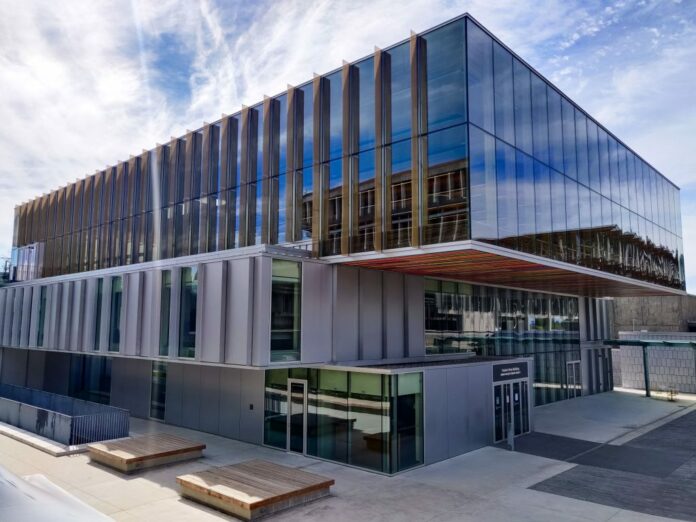 This is a photo of the SFSS building on a bright, sunny day, where the glass of the building reflects the blue sky and clouds.