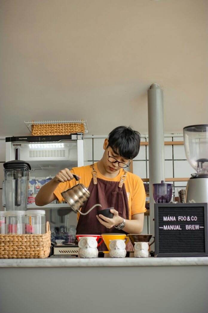 A barista in a bright yellow shirt pouring coffee behind a counter.