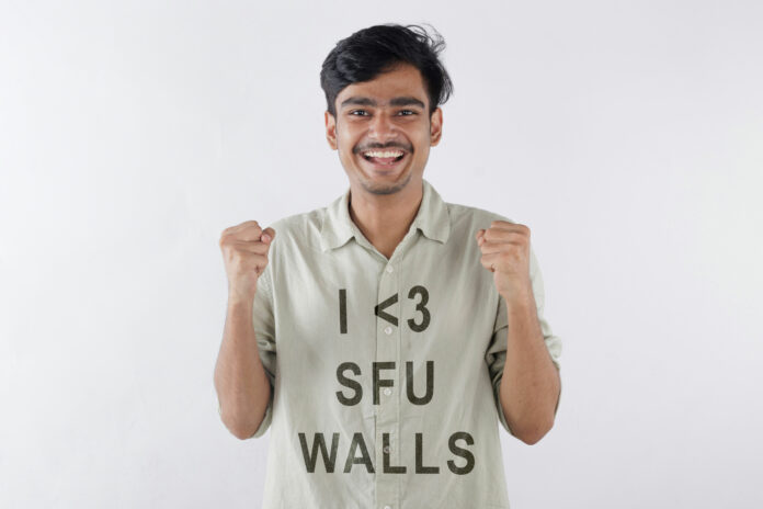 A young man wearing a green t-shirt with the text “I love SFU walls.”