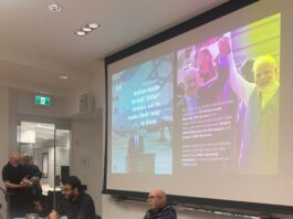 This is a photo of two men sitting at a table, one with a mic in his hand, in front of a slides presentation about the India-Israel alliance.