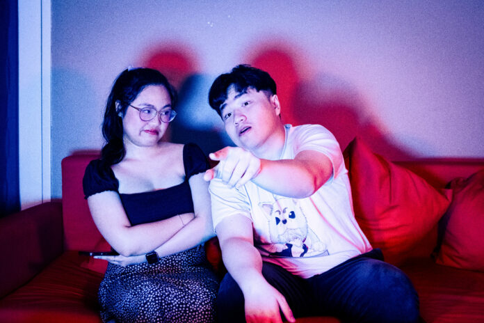 Movie-plot_emily-le a photo of two people sitting on a couch, watching a movie. One person appears to have figured out the plot, while the other is annoyed.