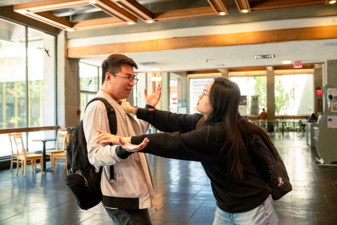 A man shoving a woman out of the way in the hallway of the Academic Quandrangle.