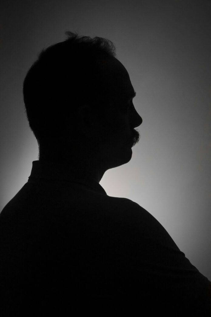 This is a black and white photo, composed so that only a man’s black silhouette is visible in front of a white, grey, and black gradient in the background.