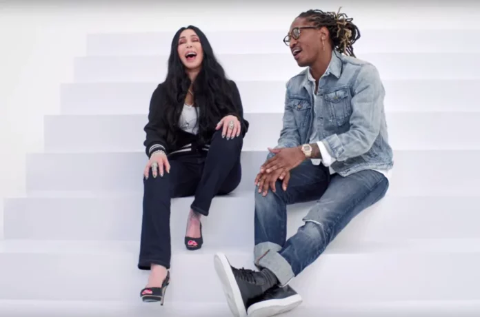 Cher and Future perched upon a white set of stairs in a white abyss. Both have their mouths open, indicating they are singing.