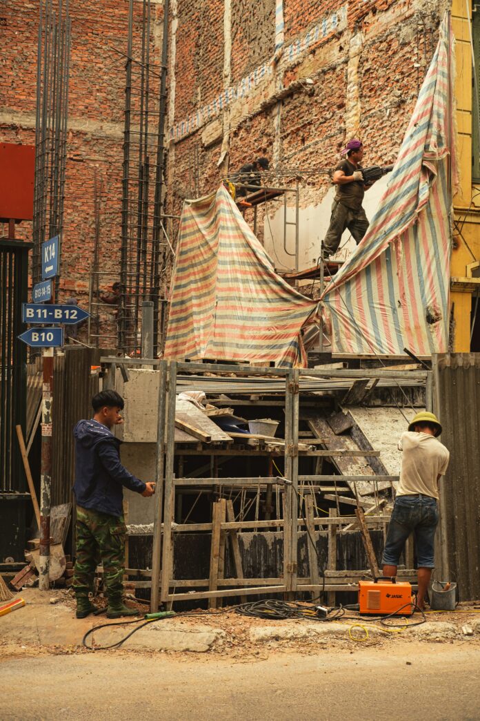 manual_labour_Nguyễn_Hiệp This is a photo of three men doing manual labour outside on metal scaffolding.