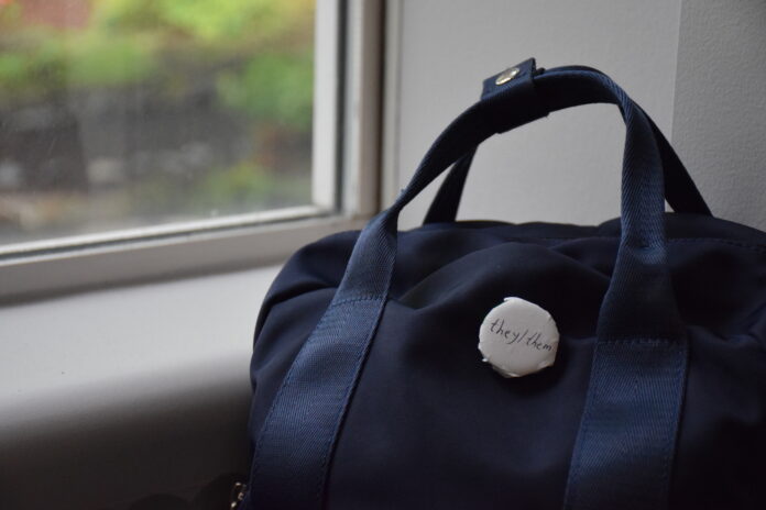 A white pin on a navy duffel bag that says “They/them”