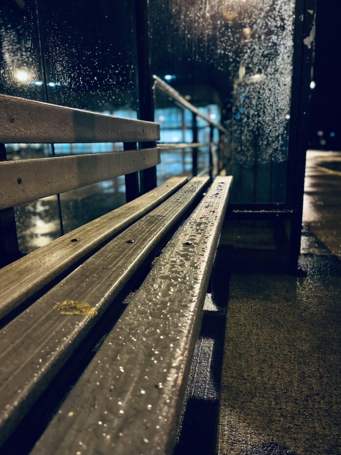 A photo of a drenched bench under the rain.