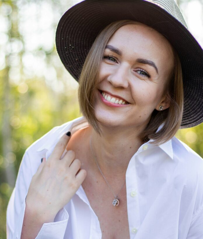 yana-tsybrovska_white-lady_unsplash A middle-aged woman wearing a black sunhat and a oversized white dress shirt. Her nails are black and she is in a field of some sorts.
