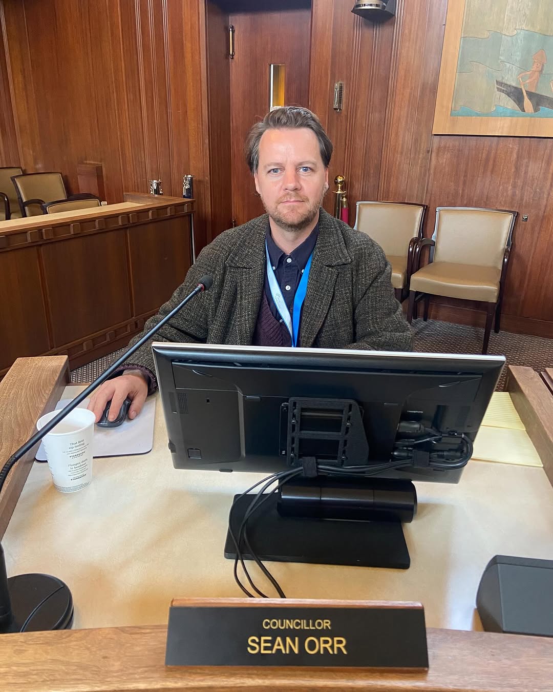 A photo of Sean Orr sitting on a desk, a name tag in front of him.