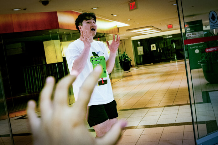 A picture of a man with a frightful face in front of the SFU Harbour Centre campus (inside of the mall). A hand is reaching towards him.