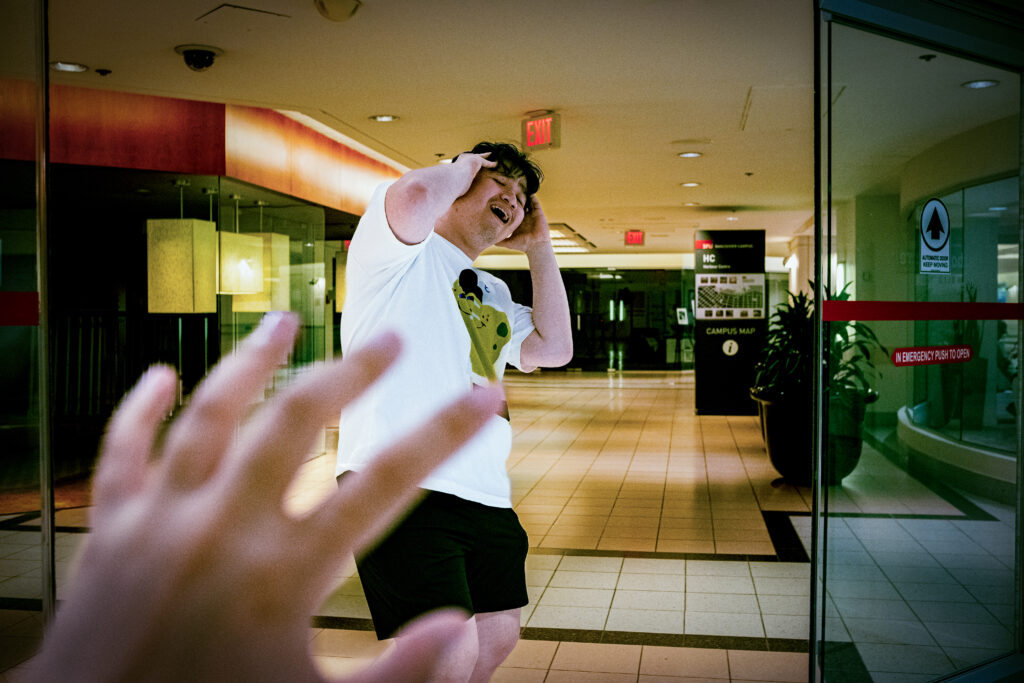 A picture of a man with a frightful face in front of the SFU Harbour Centre campus (inside of the mall). A hand is reaching towards him. 