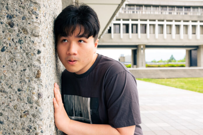 A man pressing his ear against a wall at SFU. He is shocked at what he is hearing.