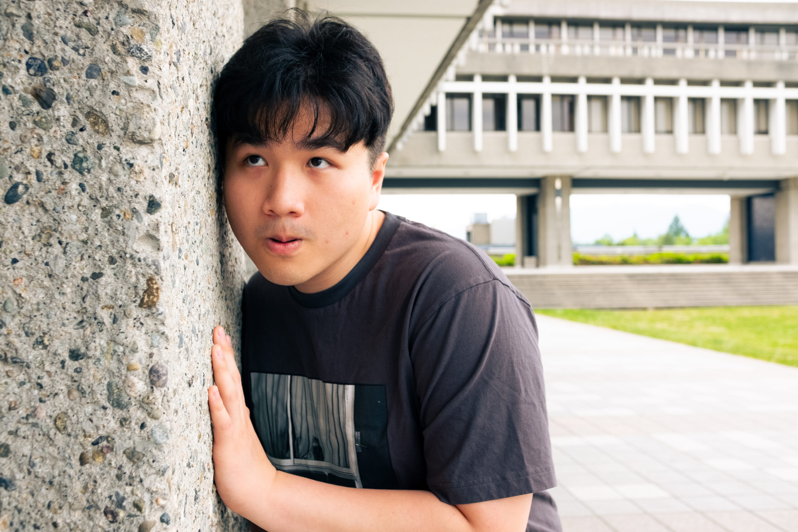 A man pressing his ear against a wall at SFU. He is shocked at what he is hearing.